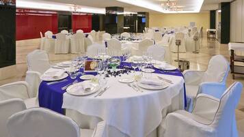 A banquet hall with round tables, white chairs, and blue tablecloths.