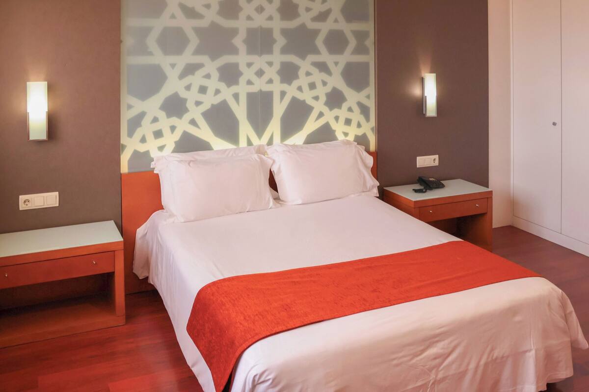 A hotel room with a bed, two nightstands, a telephone, and a patterned wall.