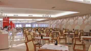 A spacious dining area with multiple tables and chairs, a bar area, and a large chandelier.