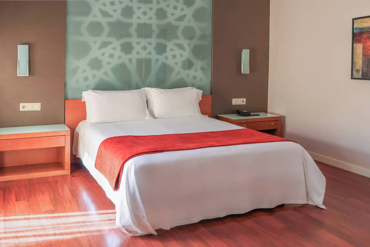 A hotel room with a bed, nightstands, a telephone, and a patterned wall.
