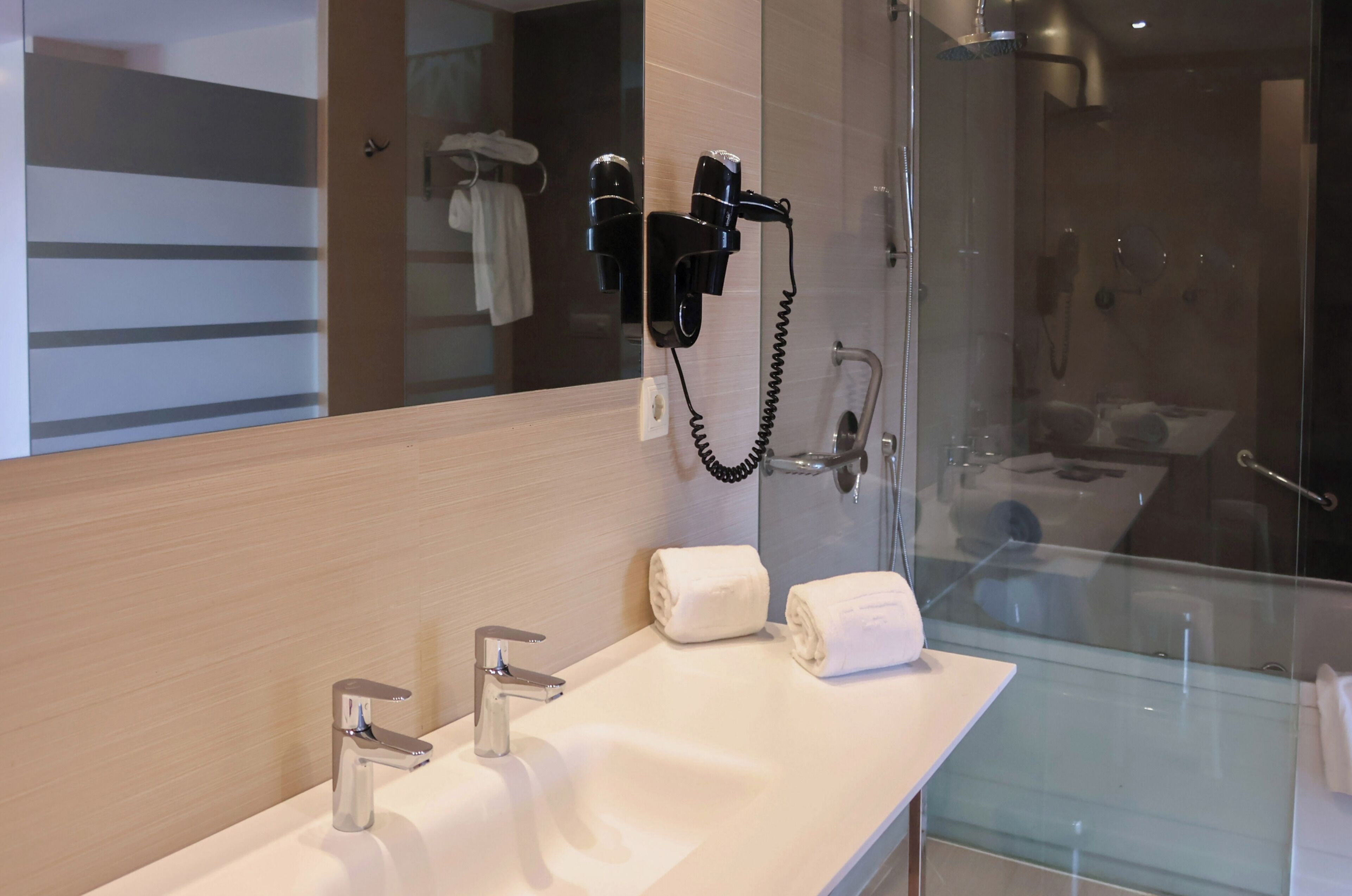 A modern bathroom with a glass shower enclosure, a vanity with a mirror, and two hair dryers mounted on the wall.