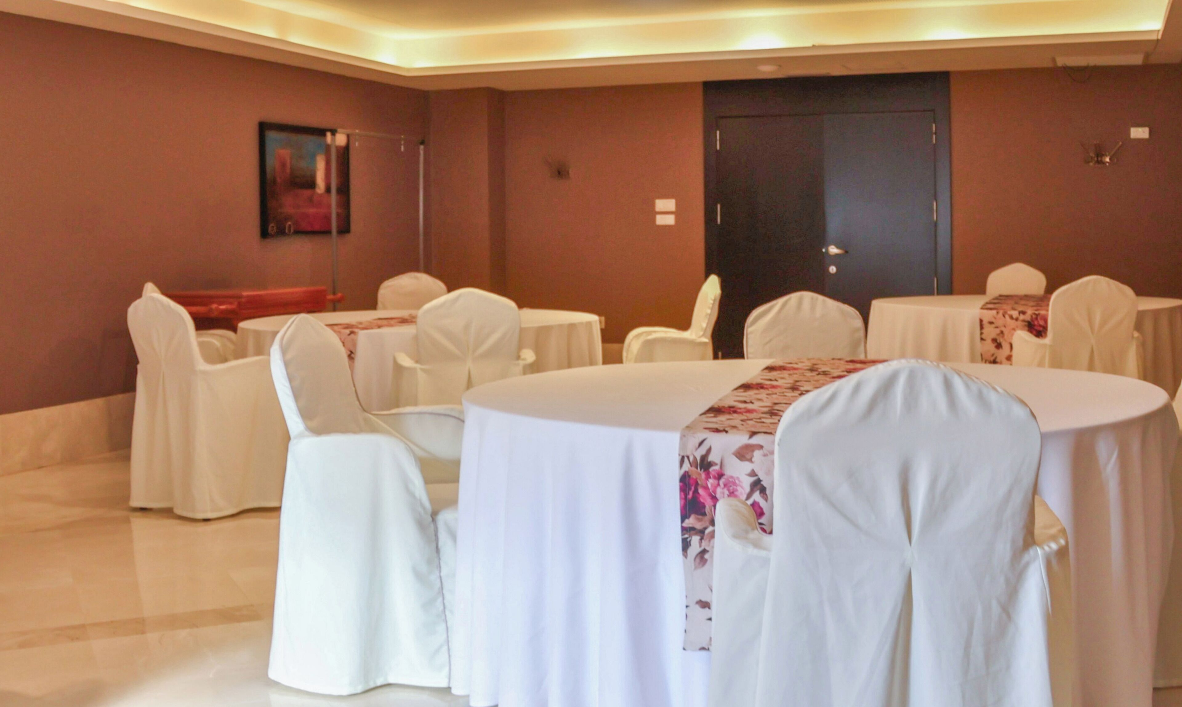 A conference room with round tables, white chairs, and a door in the background.