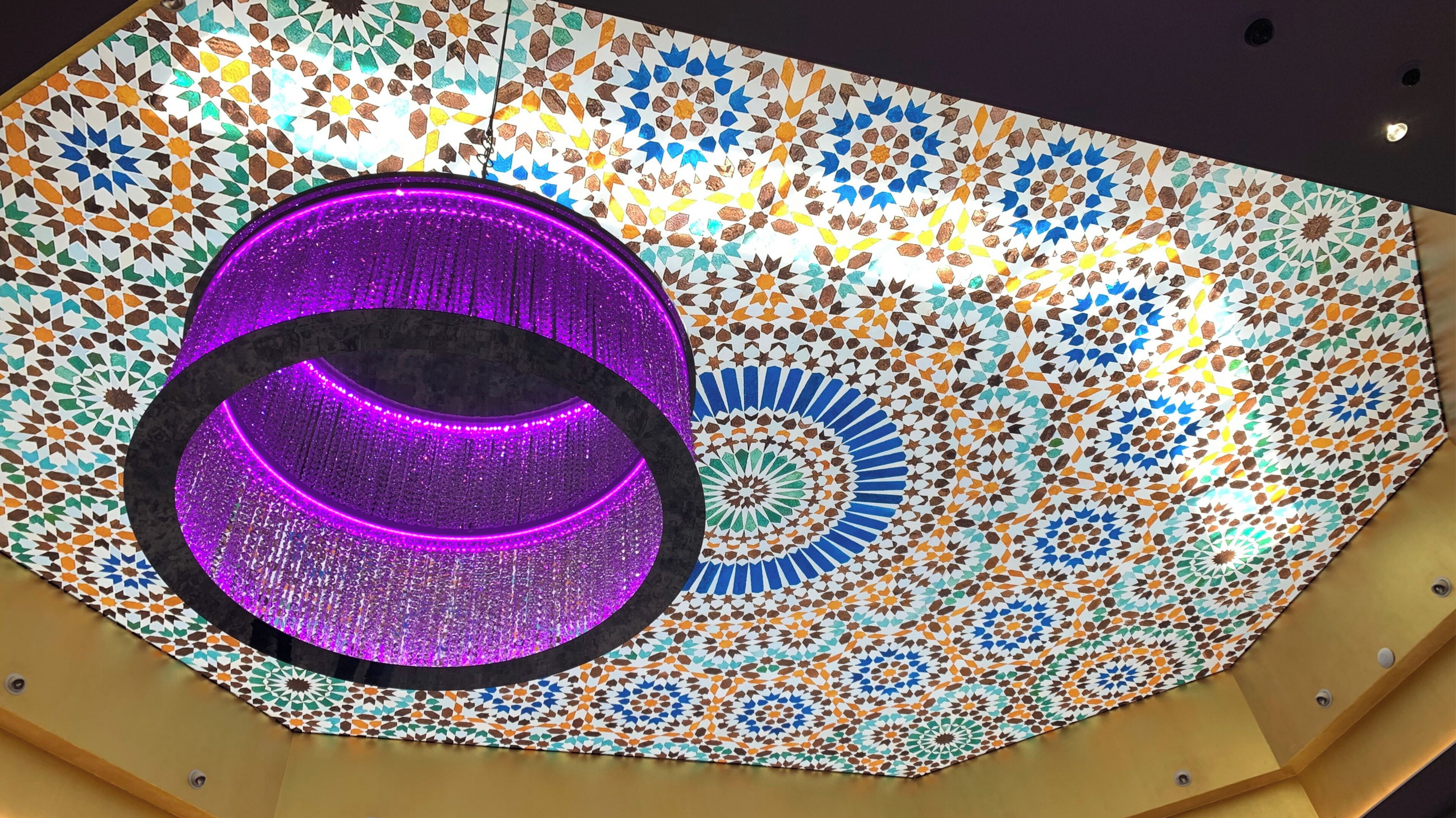 Un plafond orné d’un motif géométrique et d’un luminaire circulaire.