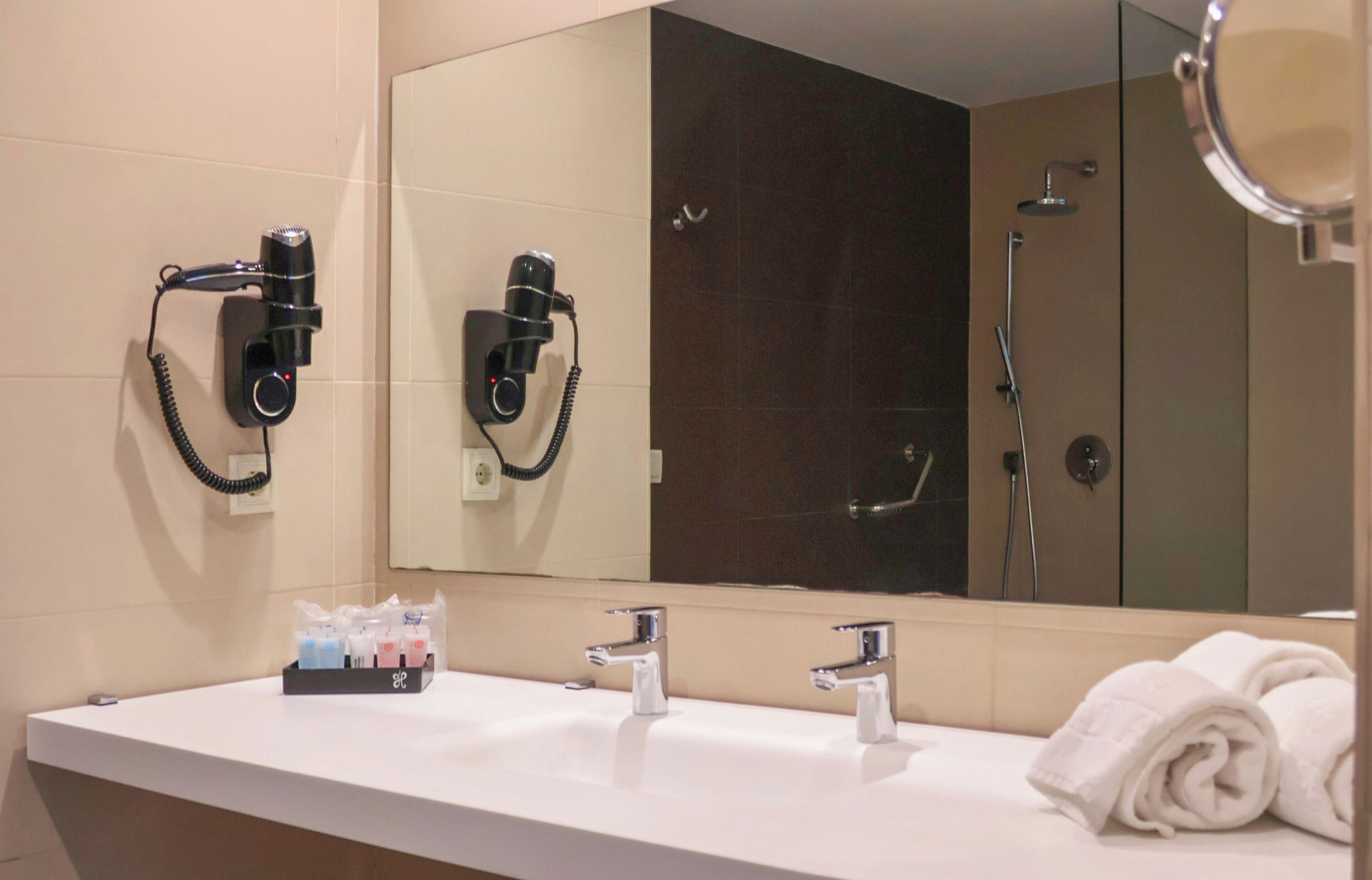 Un baño con un lavamanos blanco, dos espejos, un secador de pelo y una toalla.
