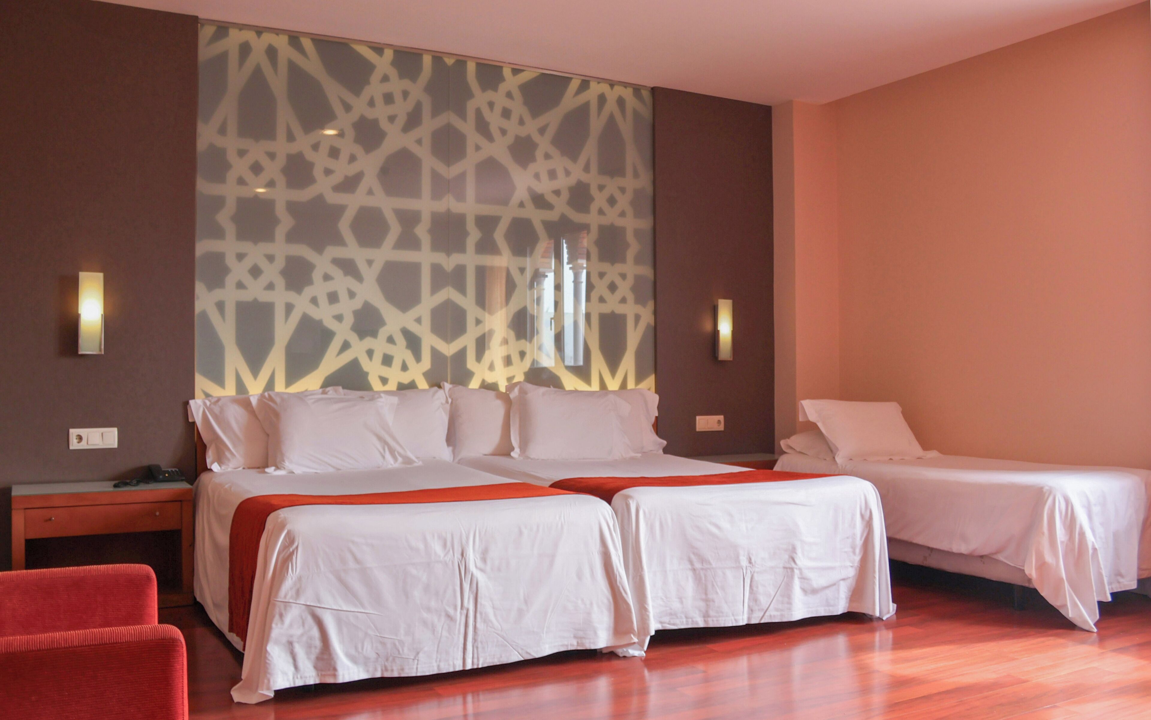 Habitación de hotel con dos camas, una silla roja, suelo de madera y decoración mural con estampado.