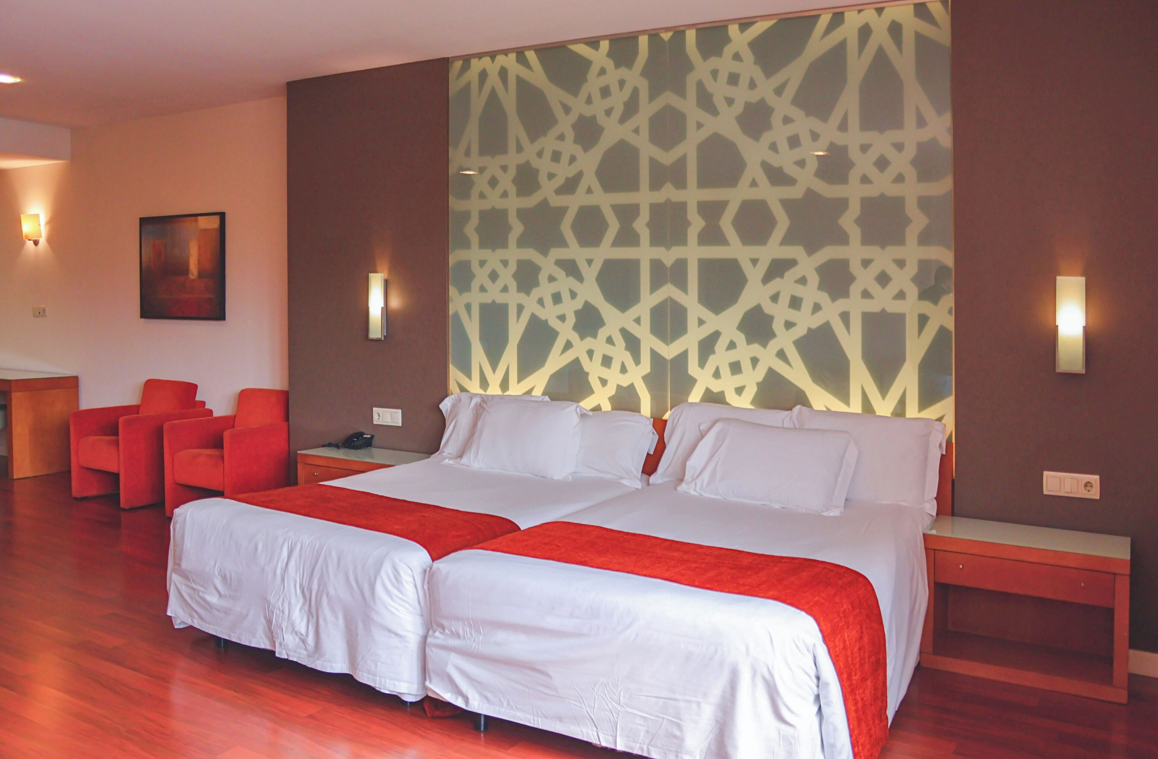 Un lit double avec du linge de lit blanc, une touche de rouge, un mur à motifs et une chaise rouge.