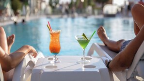 Deux personnes se détendent à une table près de la piscine, avec des boissons, et la vue porte sur une piscine.