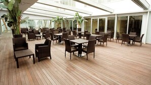 An indoor patio area with wooden flooring, tables, and chairs arranged for dining. - Hotel Cube (Ravenna)
