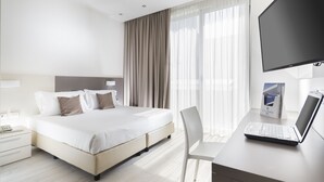 A modern hotel room with a large bed, a desk with a laptop, and a TV. - Hotel Cube (Ravenna)