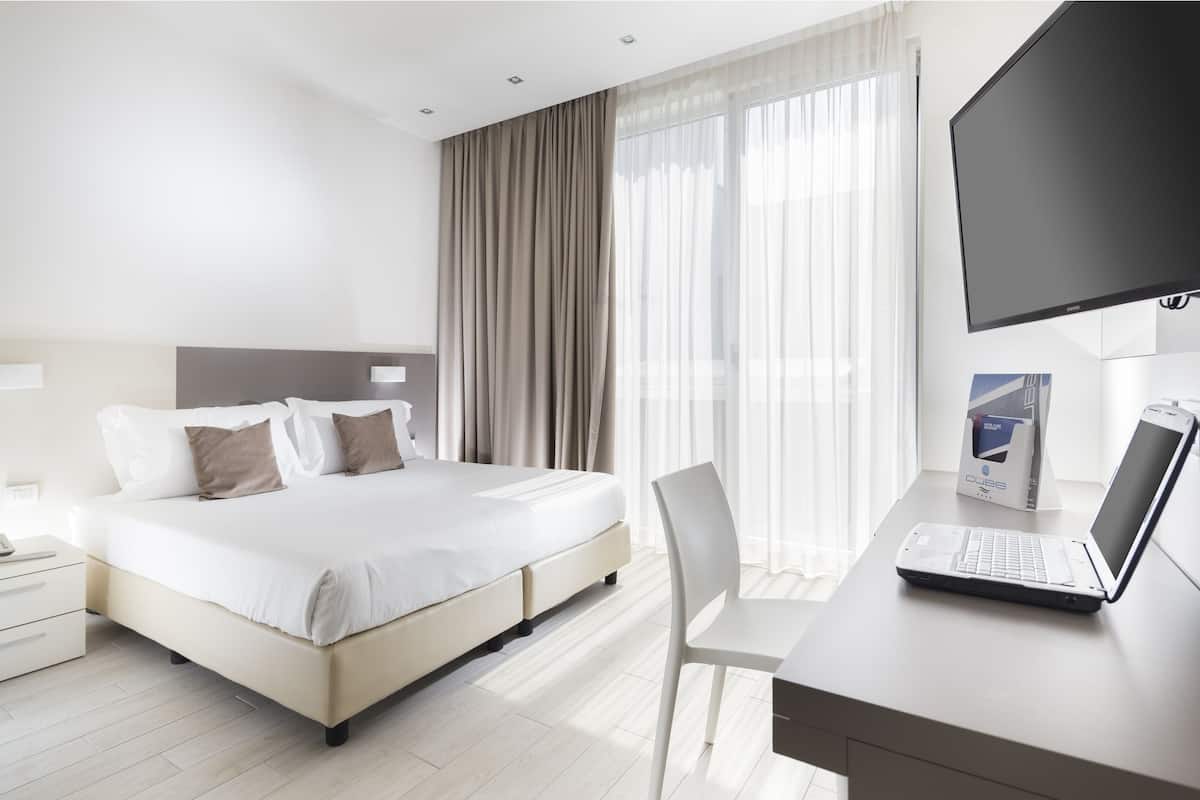 A modern hotel room with a large bed, a desk with a laptop, and a TV.