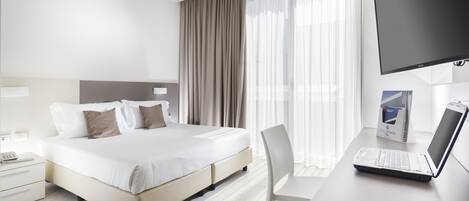 A modern hotel room with a large bed, a desk with a laptop, and a TV.