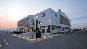 A modern hotel with a prominent sign, a parking lot, and a clear sky. - Hotel Cube (Ravenna)