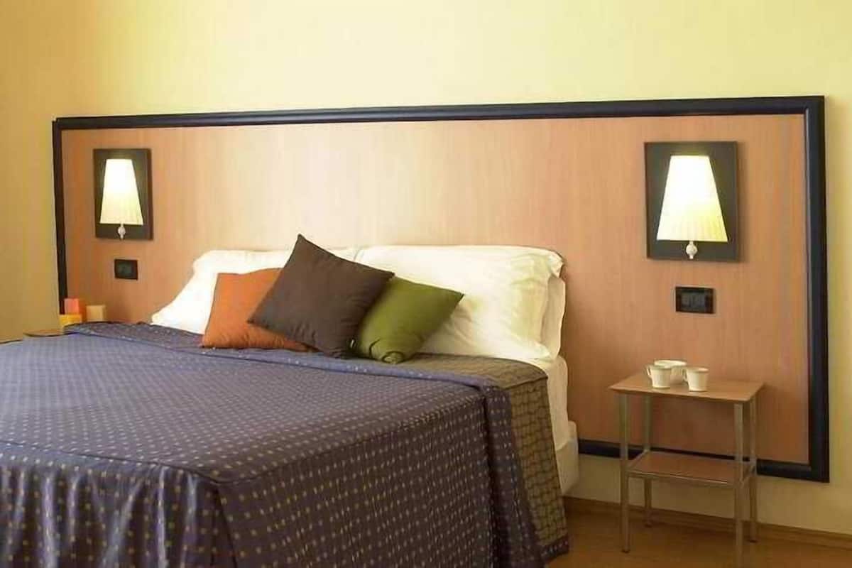 A hotel room with a large bed, a nightstand, and two wall-mounted lamps.