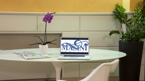 A laptop on a white table displaying "MASANI HOTEL" with a purple orchid and a potted plant beside it. - Masini Hotel (Forlì)