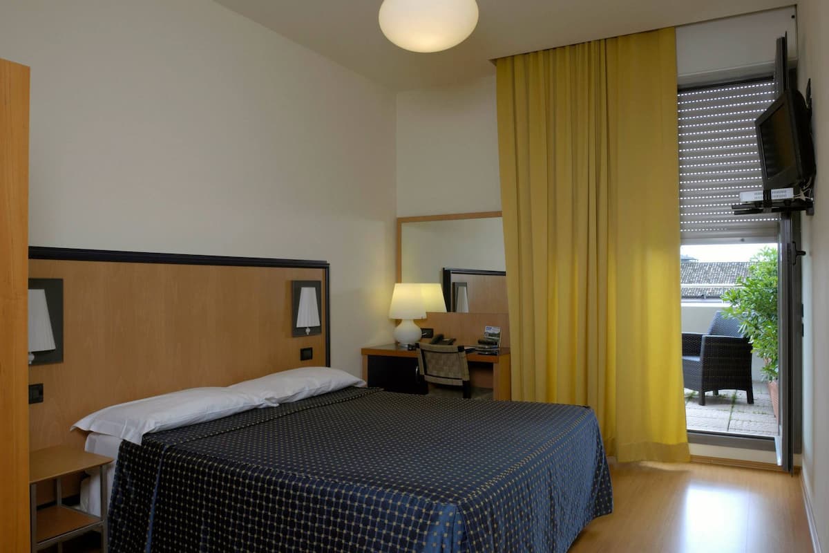 A hotel room with a bed, a desk with a lamp, a chair, and a television.