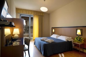 Une chambre d’hôtel comprenant un lit, un bureau avec un téléphone, une chaise, une petite table avec une lampe et un téléviseur fixé au mur.