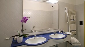 A bathroom with two sinks, a large mirror, and a hairdryer on the wall. - Masini Hotel (Forlì)