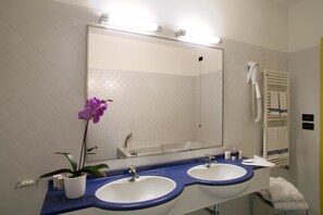 A bathroom with two sinks, a large mirror, and a hairdryer on the wall. - Masini Hotel (Forlì)