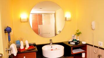 A bathroom with a round mirror, a white sink, a towel rack, a hairdryer, and a telephone.