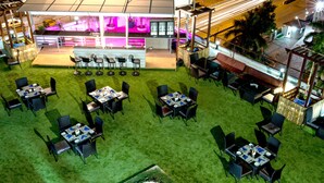 An outdoor dining area with multiple tables and chairs, a bar area with stools, and a view of the street at night. - Gokulam Park Sabari OMR Hotel (Tirupporur)