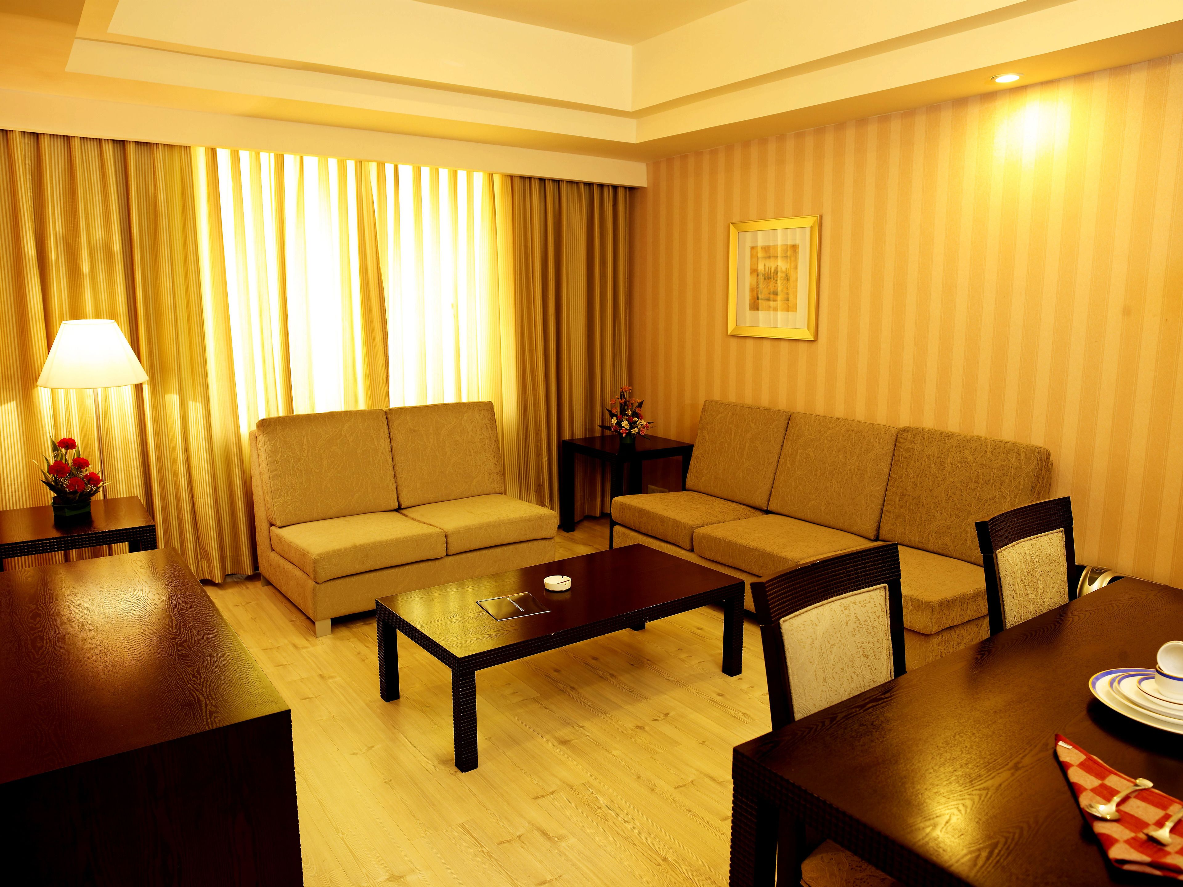 Habitación de hotel con dos sofás, una mesa de centro de madera, una mesita auxiliar con lámpara y un cuadro en la pared.