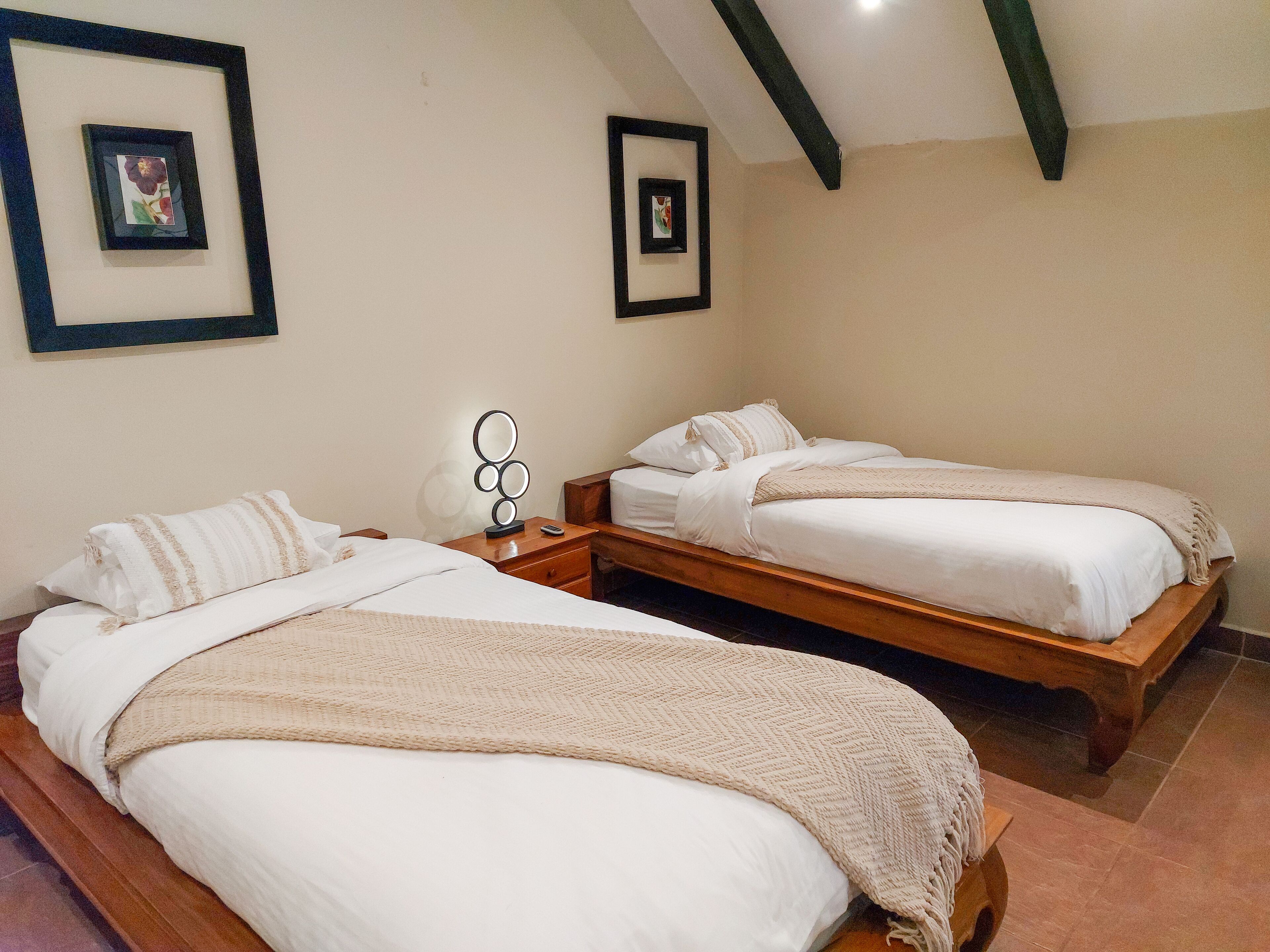 A room with two single beds, each with a wooden frame and white bedding. There are framed pictures on the wall above each bed.