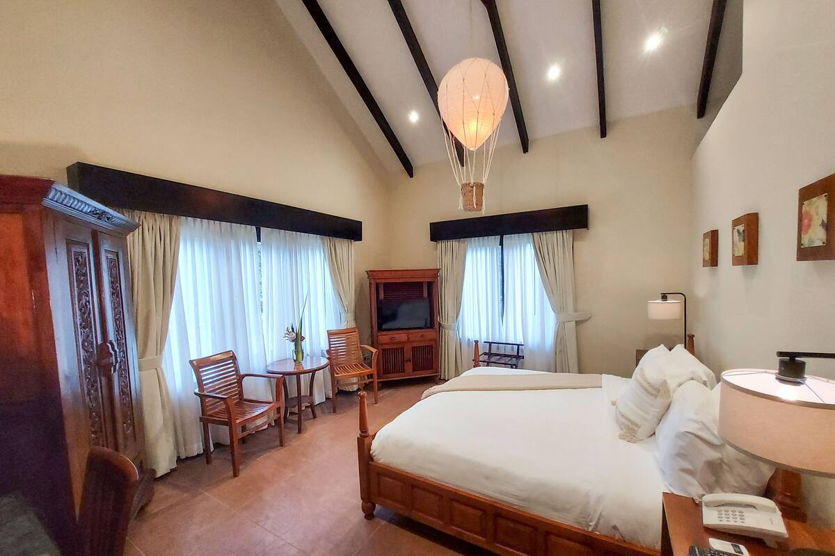 A hotel room with a large bed, wooden furniture, a television, and a desk with a lamp and remote controls.