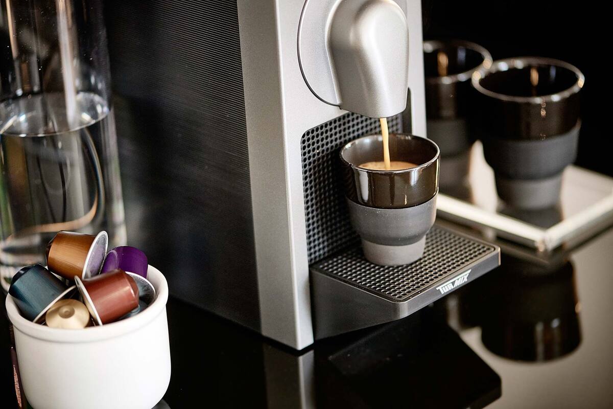 A coffee machine dispensing coffee into a cup, with a container of coffee capsules nearby.