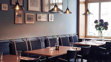 A restaurant interior with wooden tables, black chairs, and pendant lighting.
