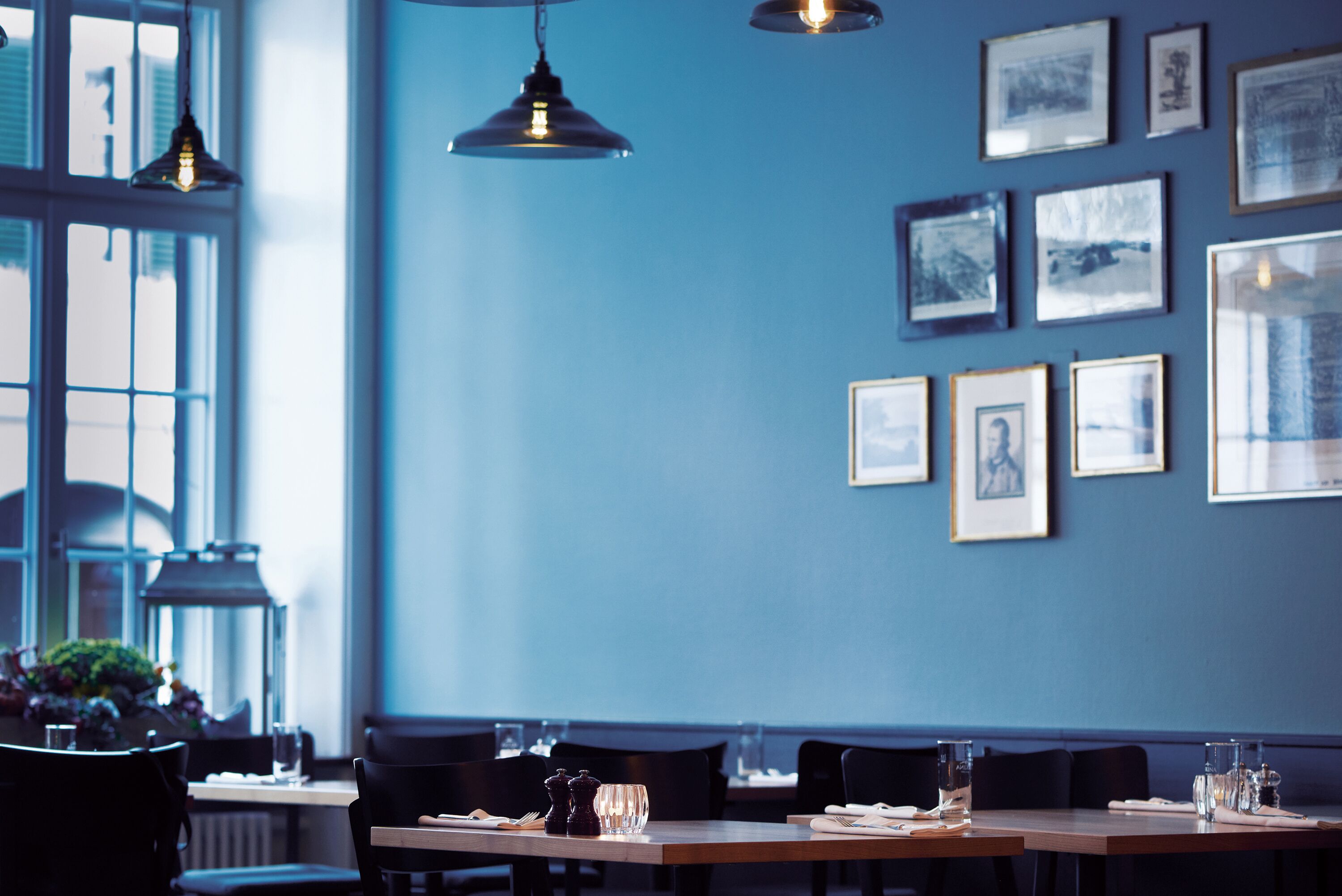 A restaurant with a blue wall, framed pictures, hanging lights, and a table set for dining.
