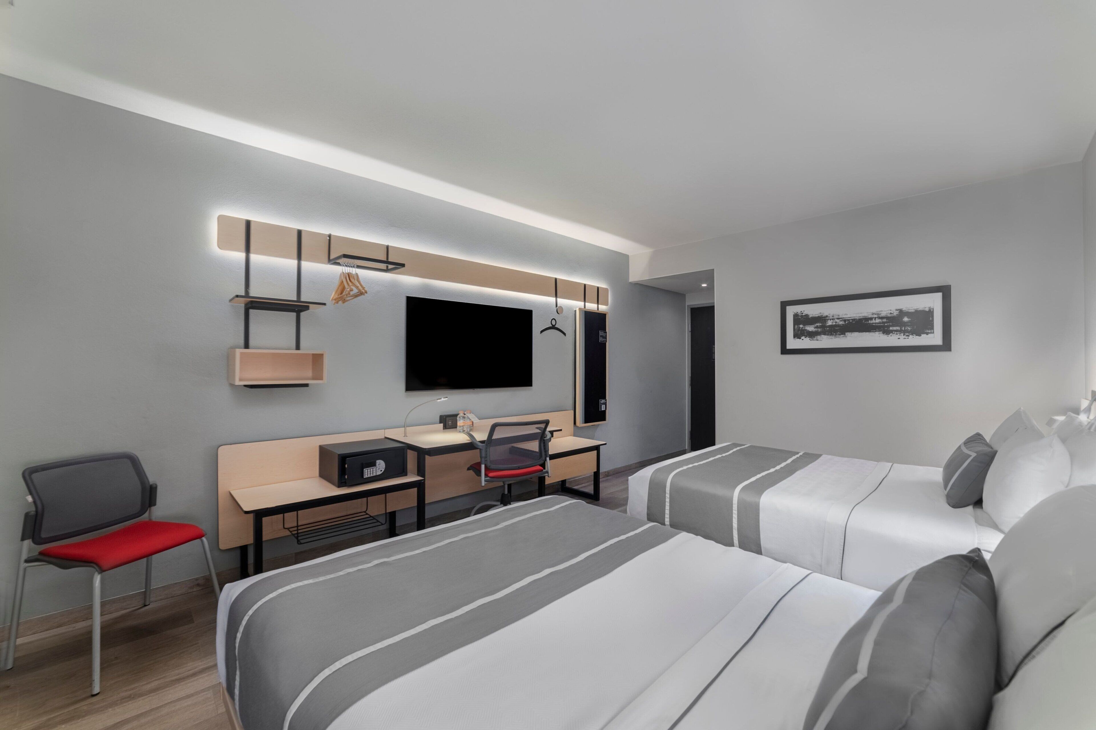 Ein modernes Hotelzimmer mit zwei Betten, einem Schreibtisch mit Stuhl, einem Fernseher und einem gerahmten Bild an der Wand.