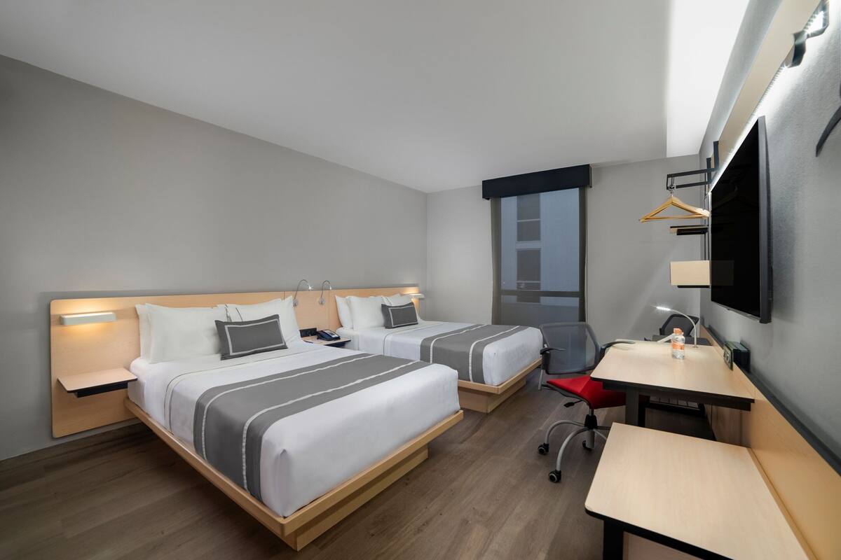 Hotellihuone, jossa on kaksi sänkyä, työpöytä, tuoli, televisio ja ikkuna.