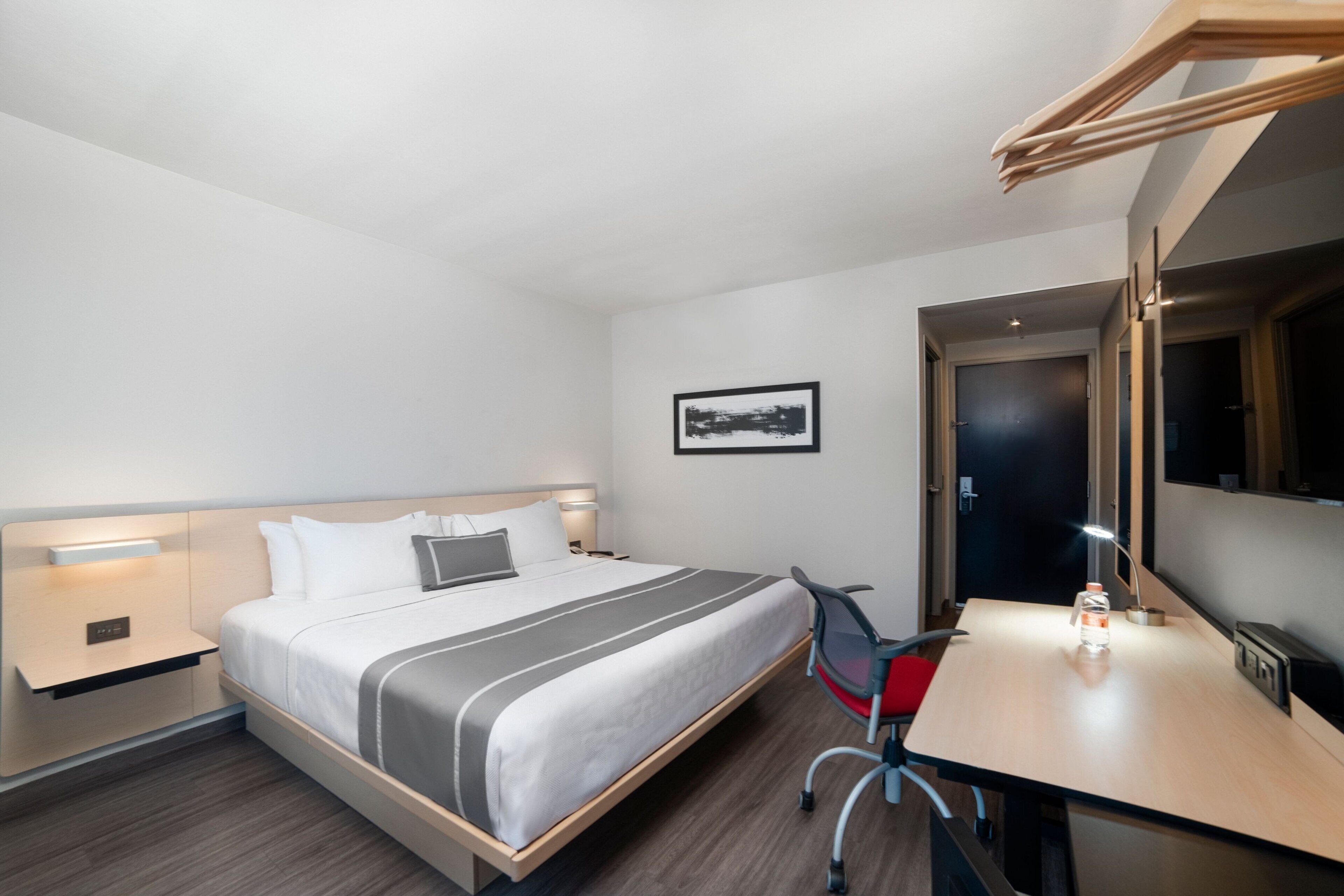 A hotel room with a bed, bedside table, desk, chair, and a mirror.