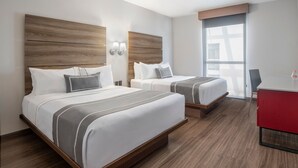 Habitación de hotel con dos camas, cabeceros de madera, un escritorio rojo y un ventanal grande.