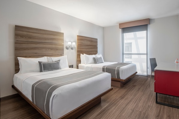 Habitación de hotel con dos camas, cabeceros de madera, un escritorio rojo y un ventanal grande.