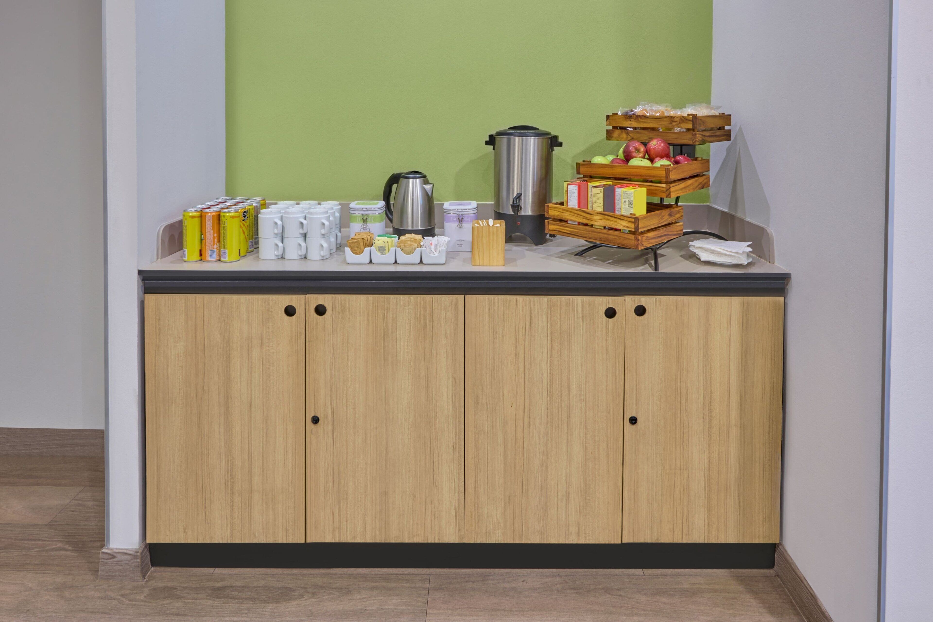 Una kitchenette con un armario de madera, una cafetera, un hervidor y una bandeja de frutas.