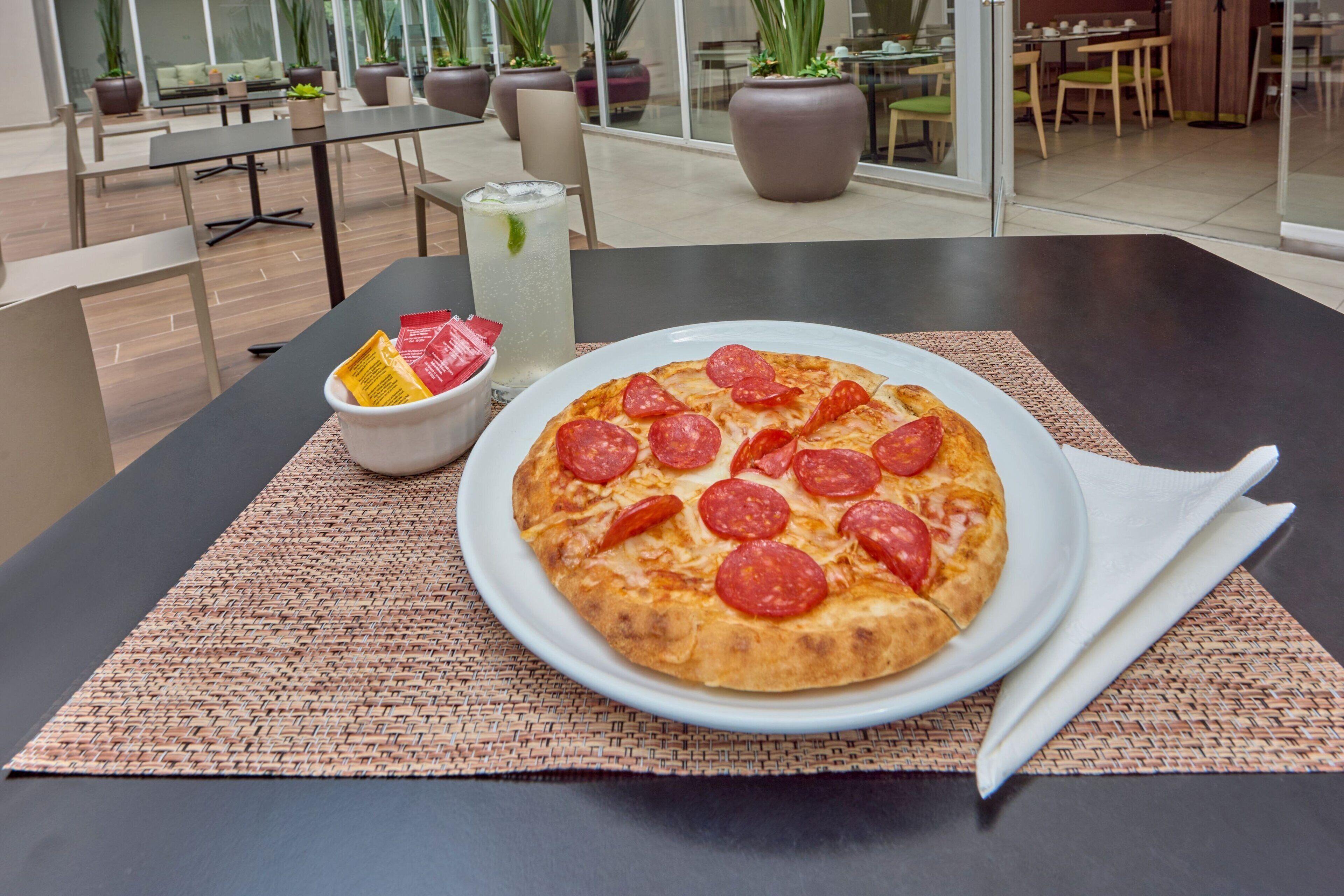 A pizza with pepperoni on a white plate on a table with a woven placemat.