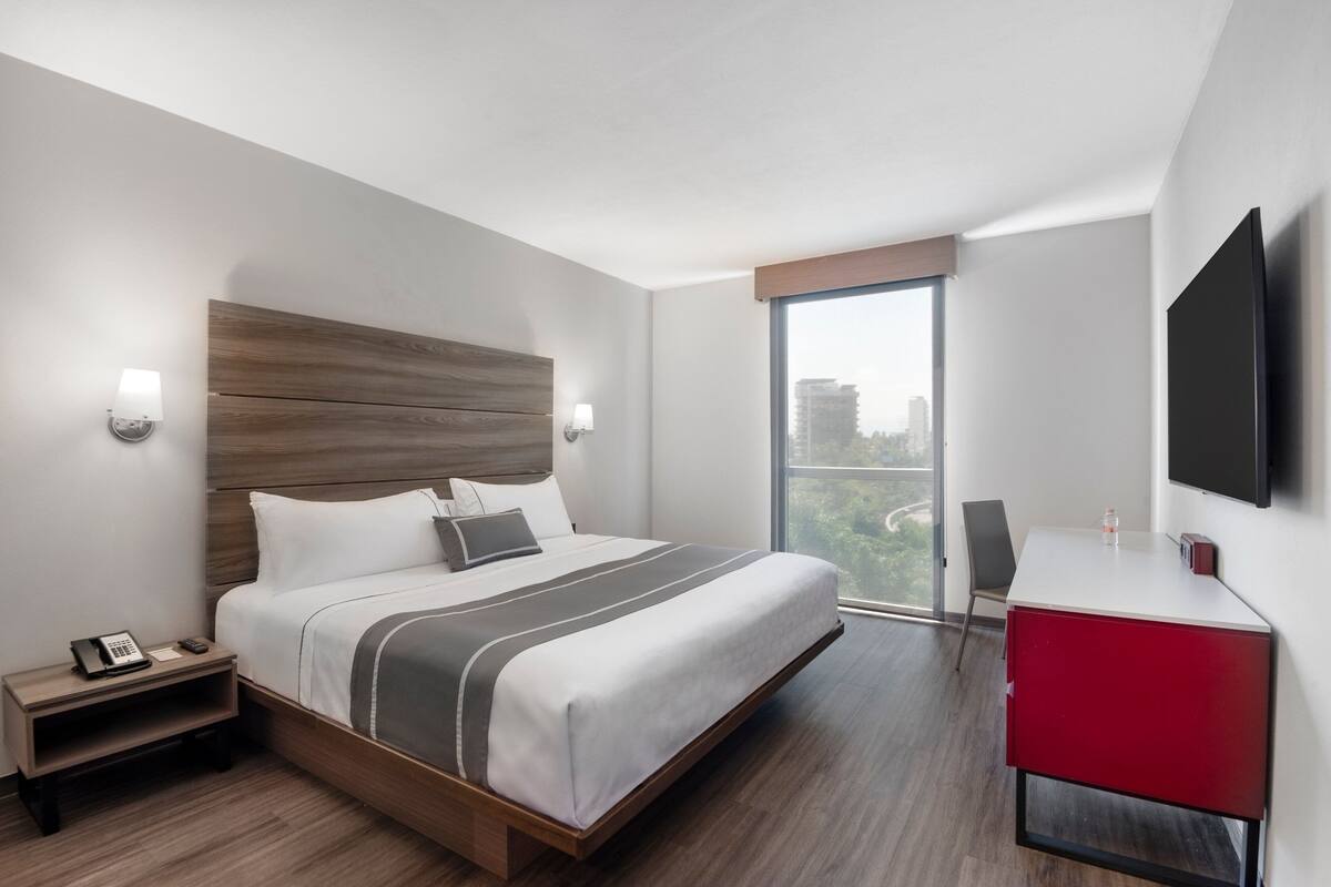 Moderni hotellihuone, jossa on suuri sänky, työpöytä ja televisio.