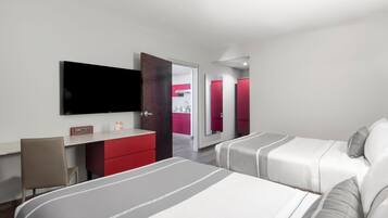 Une chambre d’hôtel moderne, équipée d’un lit, d’un bureau, d’une chaise, d’une télévision et d’une salle de bain visible à travers une porte ouverte.