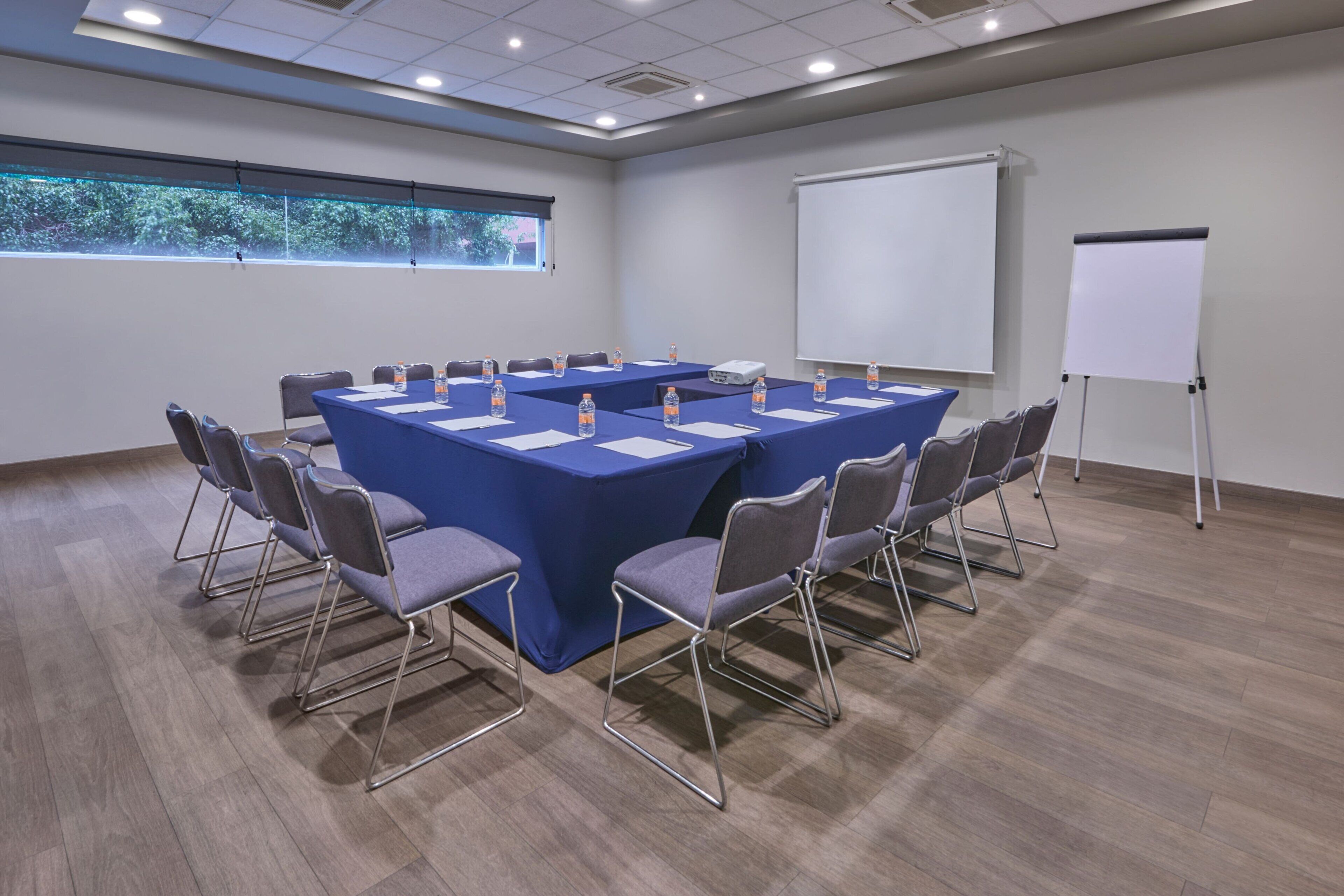 Ein Konferenzraum mit einem langen Tisch, Stühlen, einem Projektor und einer Wandtafel.