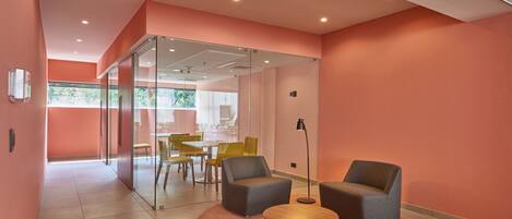 A modern interior with a glass partition, a round table, two armchairs, and a dining area with yellow chairs.