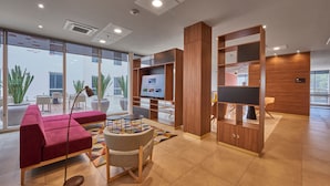 Un moderno vestíbulo de hotel con un sofá rojo, una mesa redonda, un televisor y estanterías de madera.