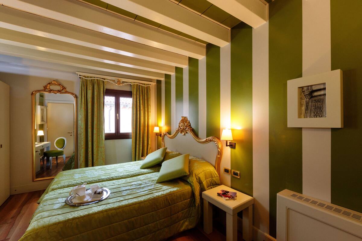 A hotel room with a bed, bedside tables, a mirror, and a radiator.