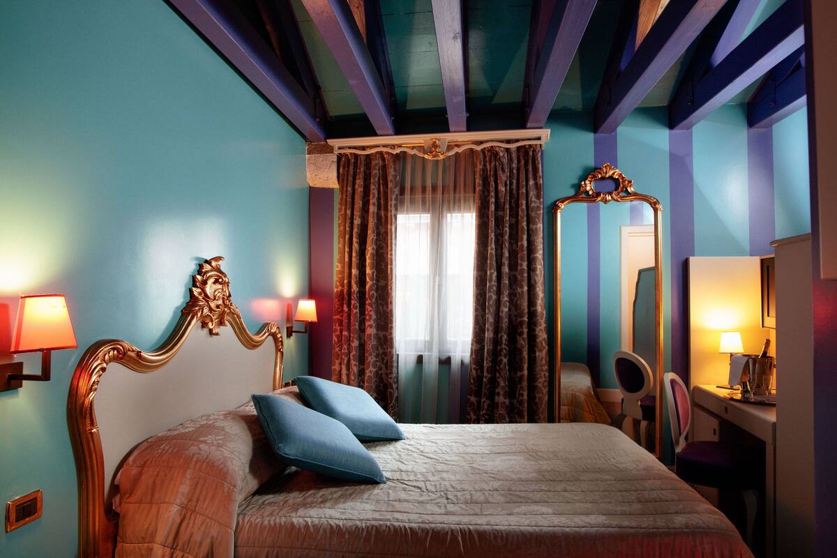 A bedroom with a bed, two pillows, a mirror, a desk with a chair, and a lamp.