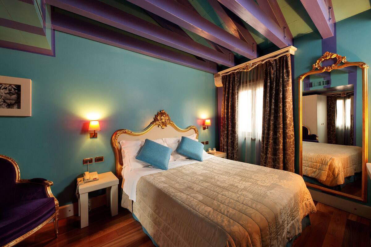 A bedroom with a four-poster bed, two bedside tables, a nightstand, a large mirror, and a framed picture on the wall.
