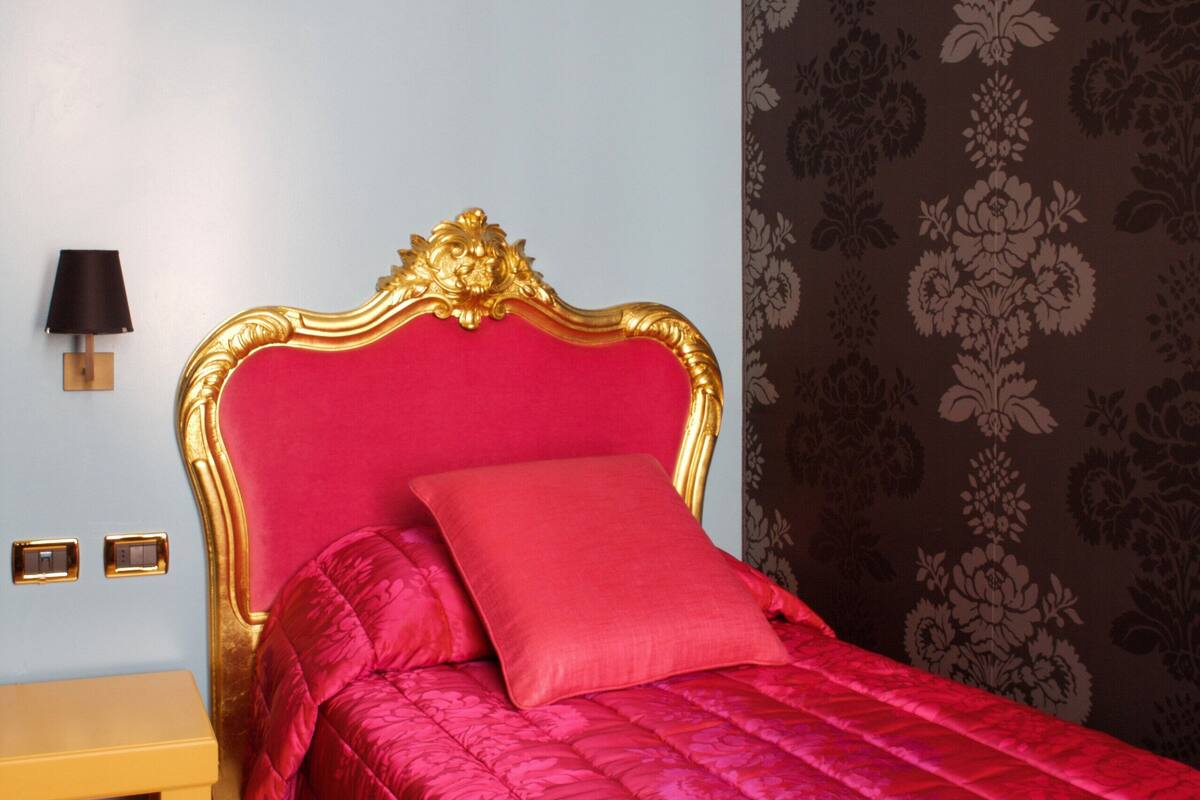 A room with a bed, a nightstand, and a wall with patterned wallpaper.