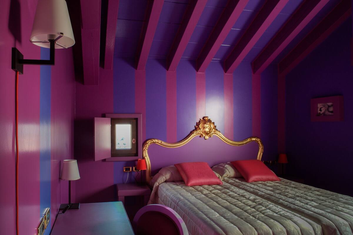 A bedroom with a bed, nightstands, a lamp, and a wall-mounted TV.