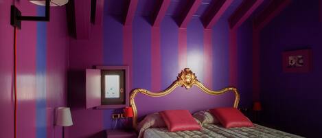 Un dormitorio con cama, mesitas de noche, lámpara y televisor instalado en la pared.