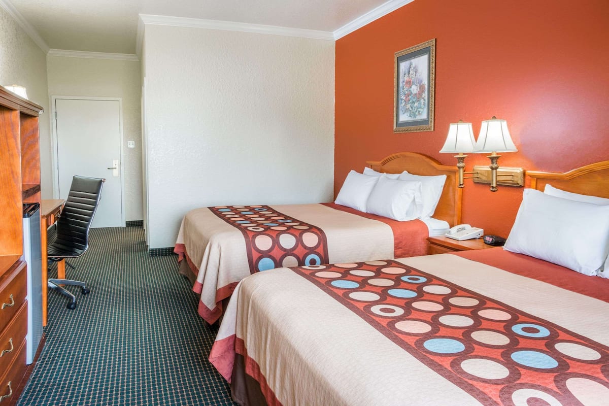Een hotelkamer met twee bedden, een bureau, een stoel, een lamp en een schilderij aan de muur.