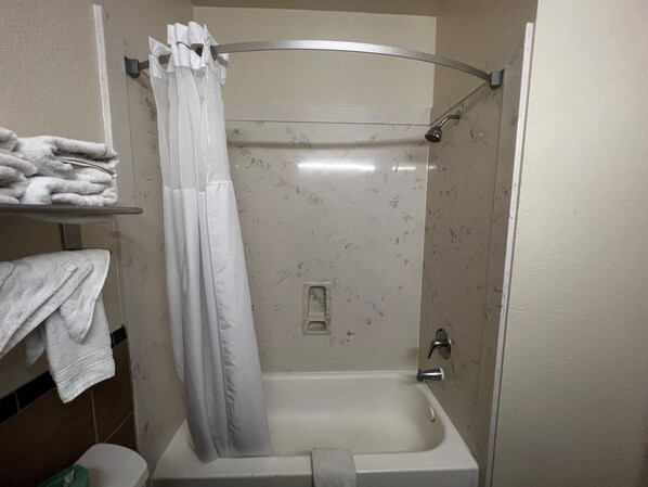 A bathroom with a shower, a toilet, and a towel rack with folded towels.